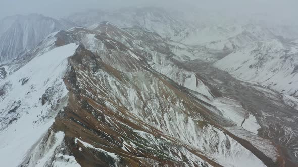 Drone Flight Over Mountain Peaks With Snow Covering One Side