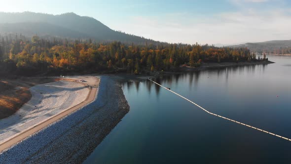 Aerial shot of a dam on a blue alpine lake surrounded by pine trees and mountains