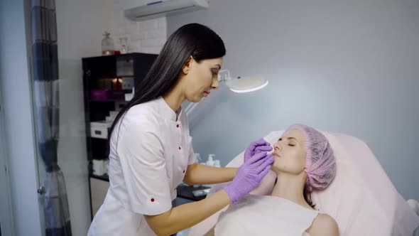 A pretty cosmetologist is looking over a shape of the client's lips