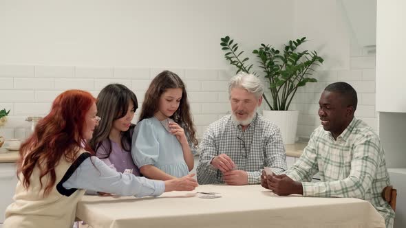 Multi Ethnic Family of Different Age Generations Play Cards at Home Sitting at the Table