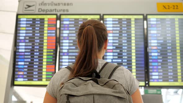 Brunette Looks at Departures Schedule in Airport Terminal