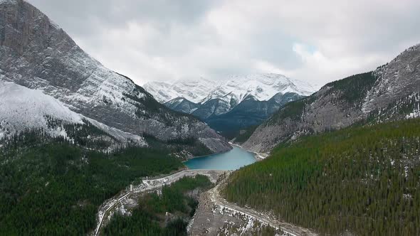 Drone rises above dense snowy forest on the slopes of massive mountains in Alberta, Canada