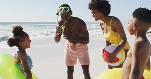 Smiling african american family with inflatables talking on sunny beach