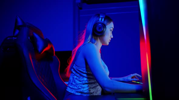 Sexy Tattooed Young Woman Sitting in Neon Gaming Club and Playing Game