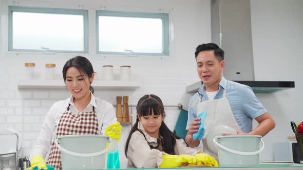 Asian young family feel happy and teaching their little kid daughter to clean kitchen room in house.