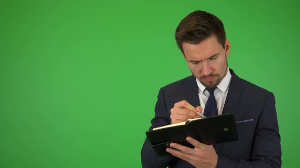 A Young Handsome Businessman Writes Into a Notebook - Green Screen Studio