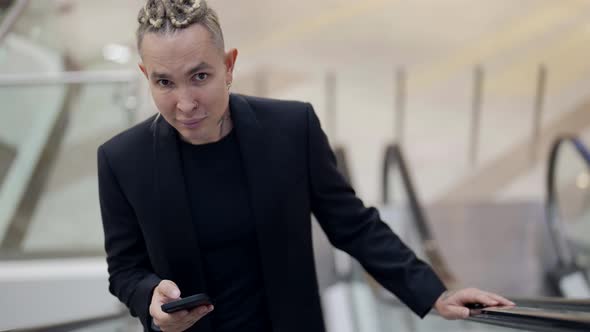 Closeup of a Beautiful Portrait of a Gay Man Riding an Escalator in a Business Center with a Phone