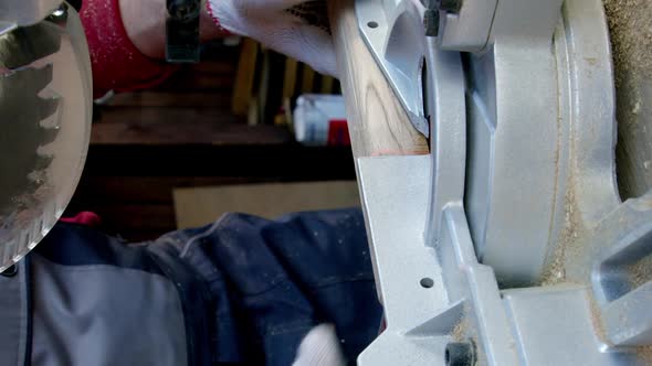 Vertical Shot Woodworker in Protective Gloves Cuts Off Piece of Wood with Mitre Saw Closeup