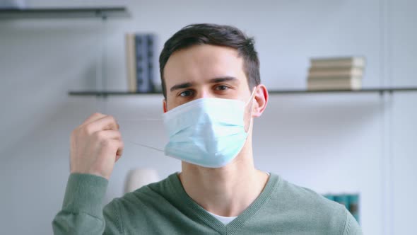 Young attractive male taking off a blue medical mask