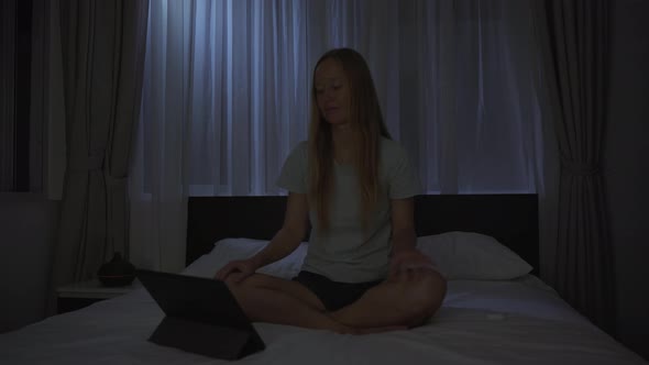 A Woman at Night Turns on a Meditation Relaxation Application on Her Tablet to Relax Before Going to