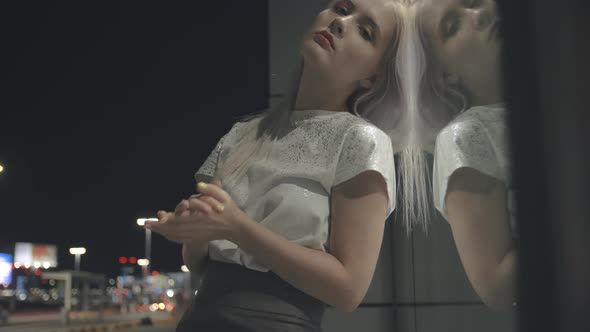 An Attractive Woman Stands with Her Back to the Glass Wall in Which She is Reflected As in a Mirror