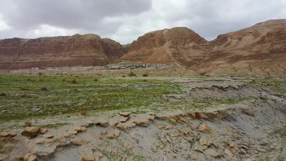 Deadsea desert hill green after the rain, fly over, red mountain and small village background, drone