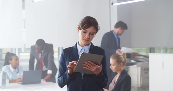 Confident Young Businesswoman Using Digital Tablet with Colleague at Background in Office