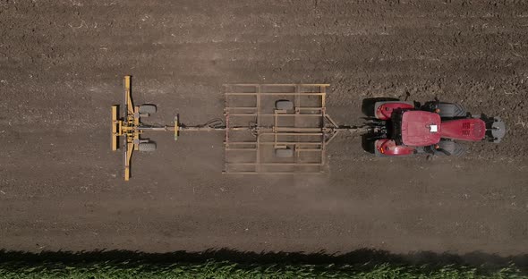 Red tractor flattening a field for seeding, Drone follow footage.