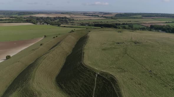 Aerial tracking down between the outer ramparts of the iron age hill fort of Maiden Castle. Sheep gr