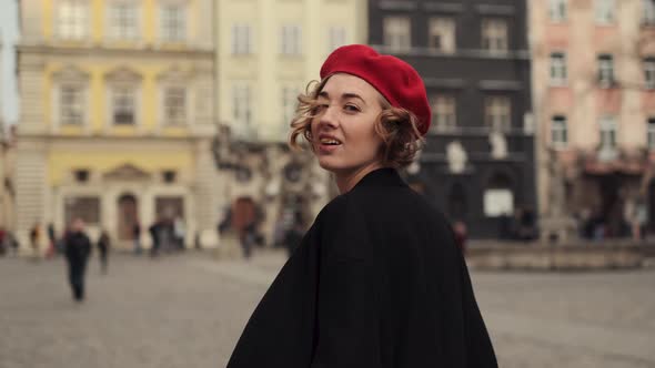 Young Woman In Red Beret Walking In City Square Smiling.