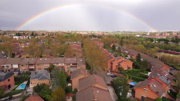 Full rainbow over residential houses in Spanish neighborhood after rain. Aerial