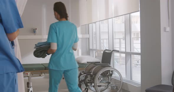 Young Nurse in Blue Uniform Gloves and Mask Changing Bedsheets of Hospital Bed in the Hospital Ward