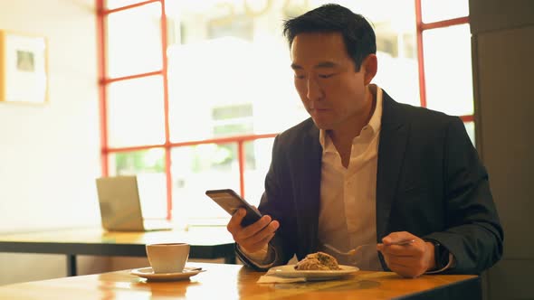 Businessman having food while using mobile phone