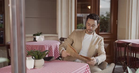 Young Man In A Festive Suit Sits Down At A Table In A Cafe