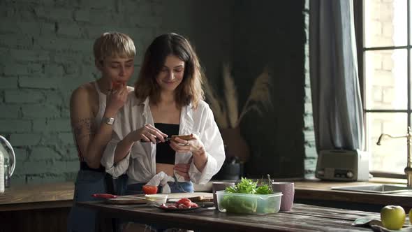 Young Lesbian Women are Kissing and Eating While Cooking Meal in Kitchen Room