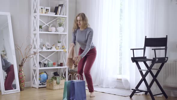 Wide Shot Portrait of Happy Young Caucasian Woman Taking Out New Dress From Shopping Bag and