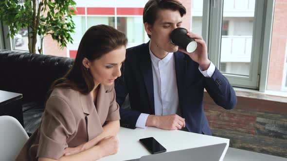 Young Man and Woman Discuss. Man Shows Details on the Screen Woman Listens Holding Cup 