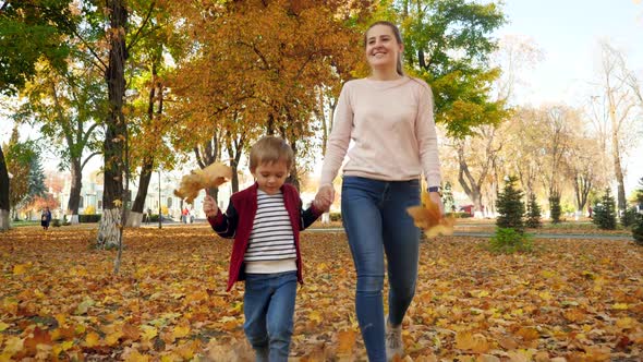 Video of Happy Smiling Mother with Little Son Walking on Grass Covered with Yellow Leaves at Autumn