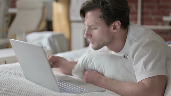 Young Man Celebrating Success on Laptop in Bed