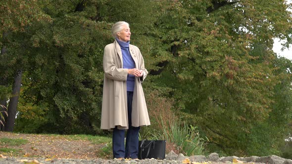 An Elderly Woman Plays Stone Skipping at a Lake and Laughs