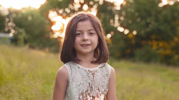 Portrait of Pretty Little Girl with Short Brown Hair Posing at Green Garden with