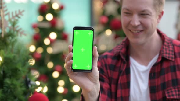 Happy Young Man Showing Phone Against Illuminated Christmas Trees Outdoors