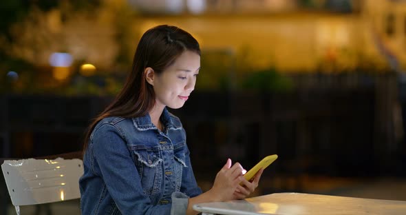 Woman use of cellphone in open air coffee shop at night