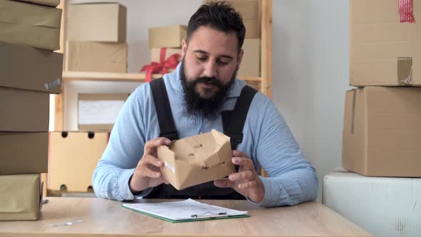 Bearded Hindu Male Business Owner Working From Home in Uniform with Packing Box at Workplace Online