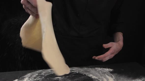 A Male Chef in in Black Clothes Twists the Dough in His Hands