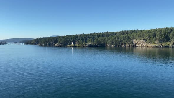 Coastline landscape view of a white lighthouse surrounded by pine trees and calm ocean water