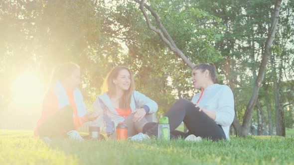 Three Girls Friends Are Sitting on the Grass After a Morning Jogging Exercise and Talking.