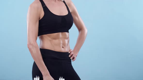 Muscular Woman in Sports Top Holds a Dumbbell in Hand a Blue Background