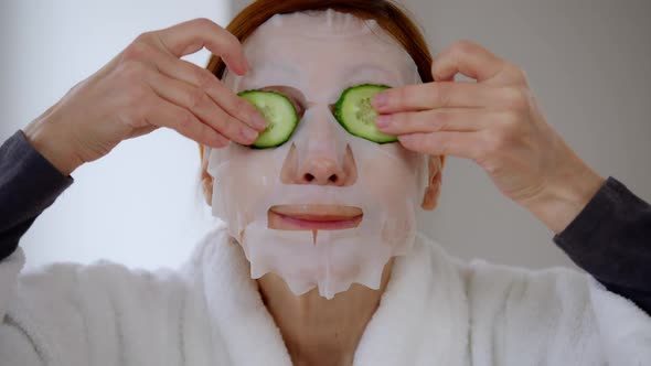 Headshot Cheerful Mature Woman in Facial Mask Putting Cucumber Slices on Eyes Laughing Looking at