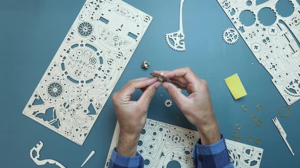 Assembling mechanical wooden puzzle toy on table. Man holding small pieces of toy in hands.