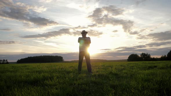 Silhouette Of Male Farmer Stands In Rural Field Against Sun Rays Of Sunset