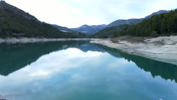 Aerial Pushout of Woman Running By Stony Shore of Lake in Guadalest