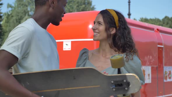 AfroAmerican Man Talks to Brunette Woman Holding Skateboard