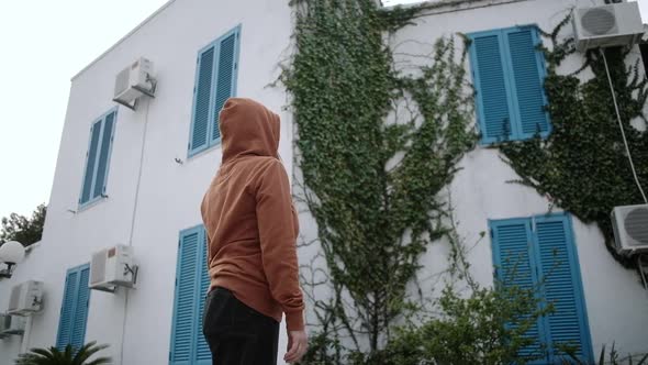 Woman in orange sweater and medical mask stay on empty street.