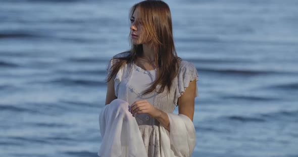 Portrait of a Thoughtful Caucasian Woman in Light White Dress Standing on the Background of Sea