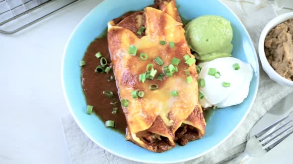 Dinner plate with Chicken enchiladas garnished with green onions and sour cream.