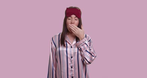 Young Bored Female in Pajamas Yawn and Shows Confusion Sign, Isolated Over Pink