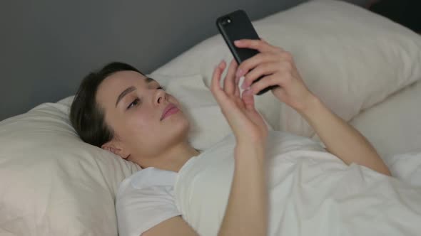Smartphone Use By Young Woman Laying in Bed