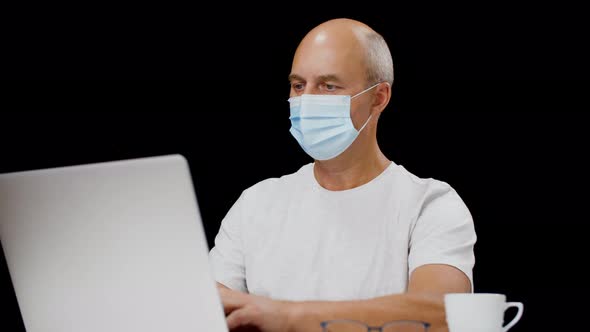 Serious Man in Medical Mask Using Laptop Computer