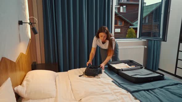 a young girl takes out her clothes from a suitcase in a hotel room